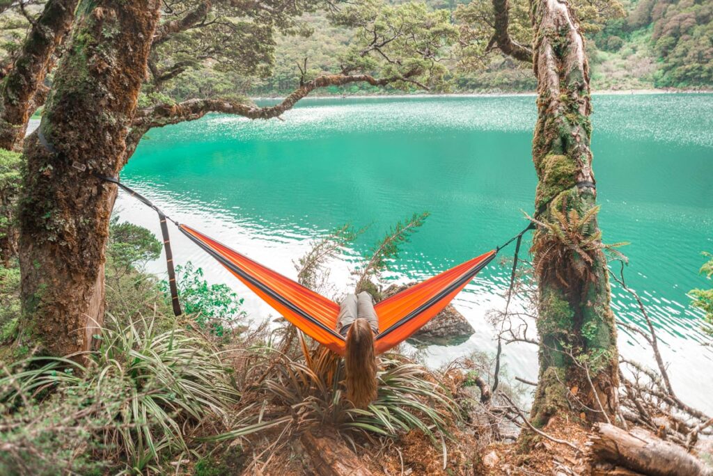 A lady sits in a hammock at Lake Mackenzie on the Routeburn Track