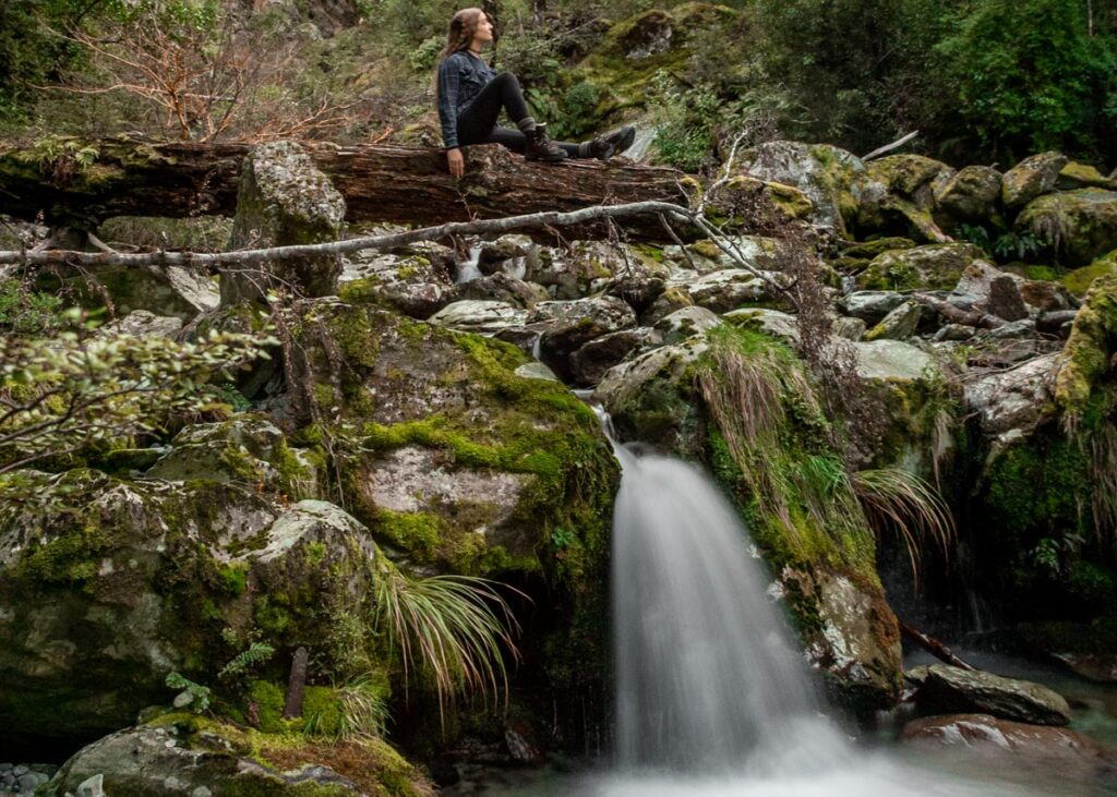 A lady sits on a log on the upper section of Bridal Veil Falls on the Routeburn Track