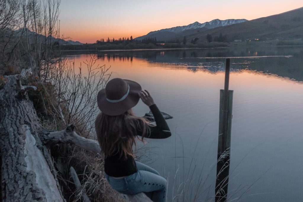 Sitting on a log on the shore of Lake hayes at sunset near Queenstown