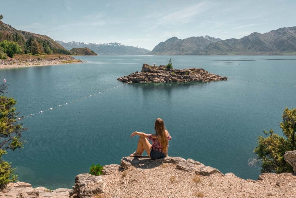 A lady sits on a cliff at Lake Hawea