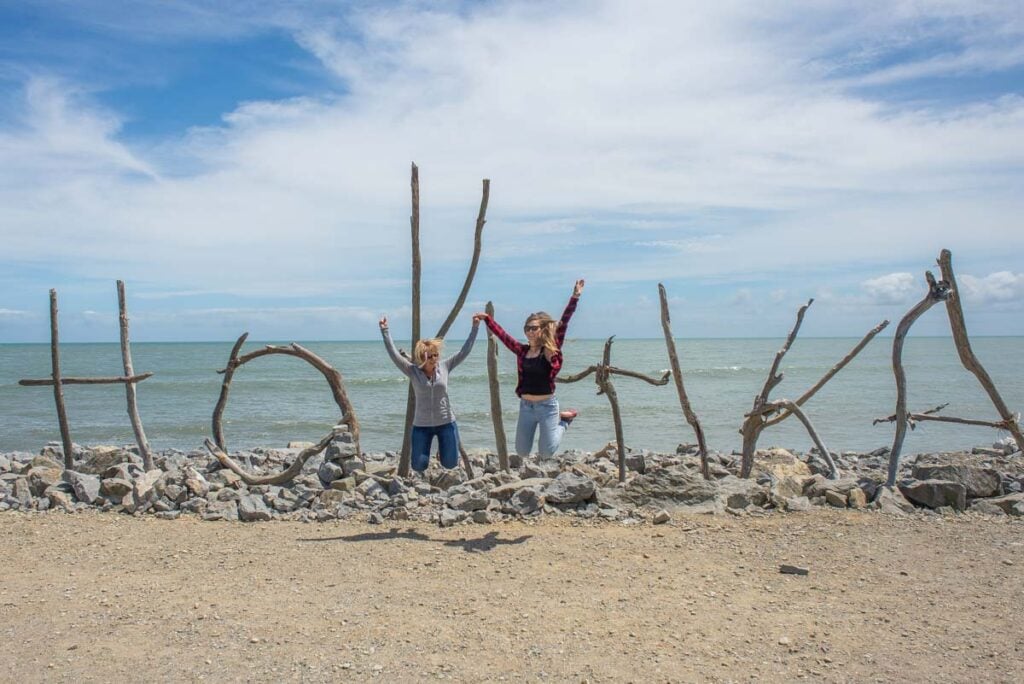 Two people jump in front of the Hokitika sign