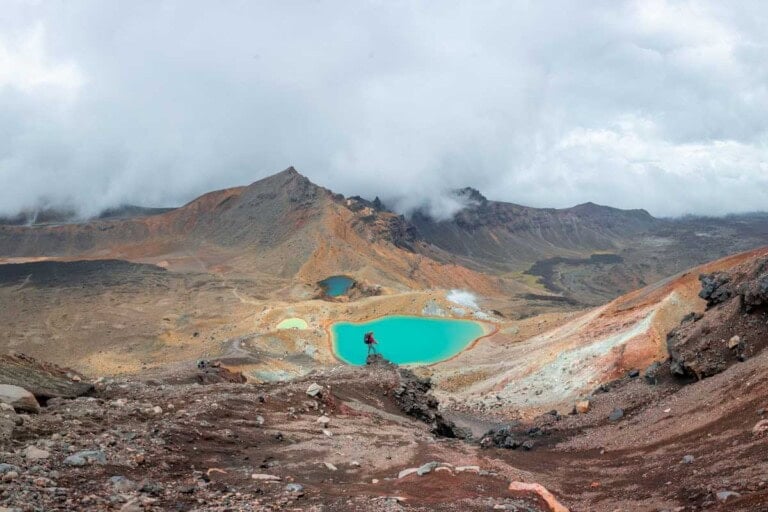 a lady stands on a rock with the view of the grren lake on the Tongariro Alpine Crossing in New Zealand