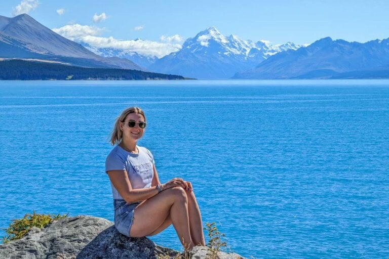 Bailey poses for a photo at Lake Pukaki with Mount Cook in the background while traveling the South Island in a rental cr