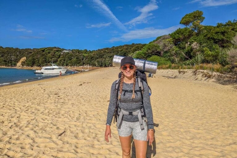 Bailey on a beach along the Abel Tasman Coastal Track in her hiking gear and large backpack with tent
