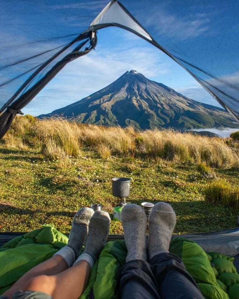 Two peoples feet and a tent while camping in Egmont National Park in NZ