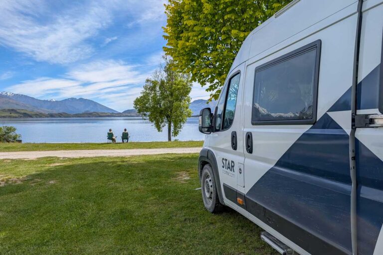 Daniel and Bailey sit by a lake with their Star RV campervan in New Zealand with the campervan nearby